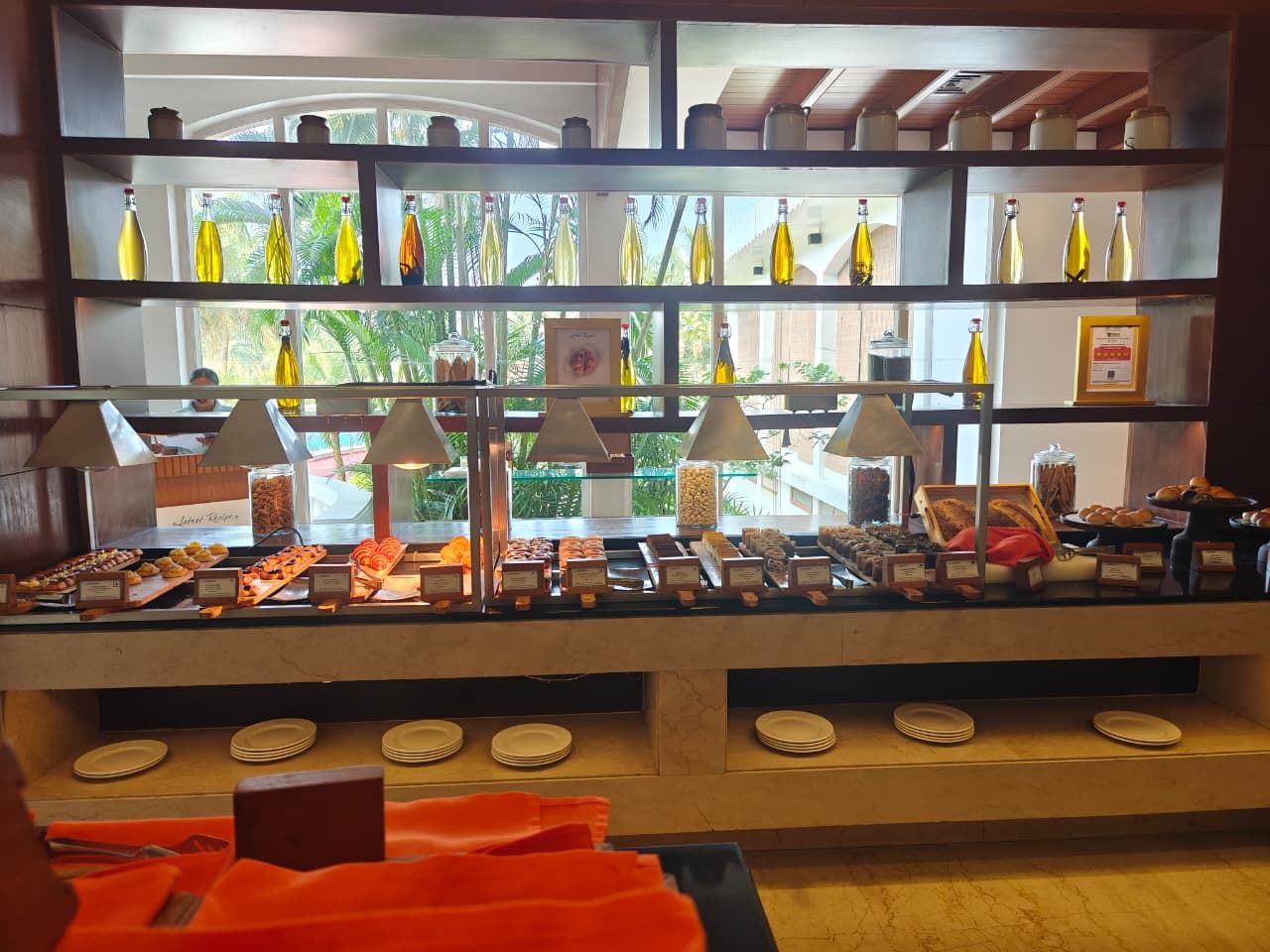 Dessert and pastry buffet spread with oil bottles on a shelf and palm trees behind