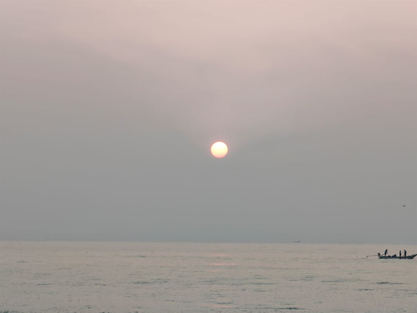 The rising sun over the water with a fishing boat in the foreground